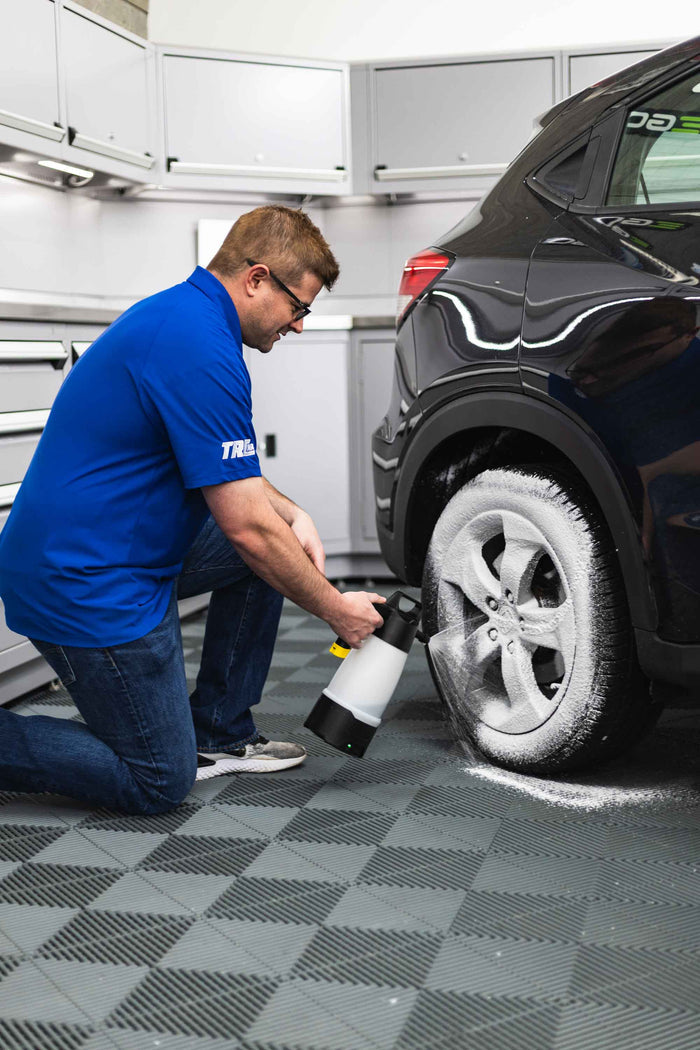 A man spraying cleaner onto a tire using an iK Foam sprayer.