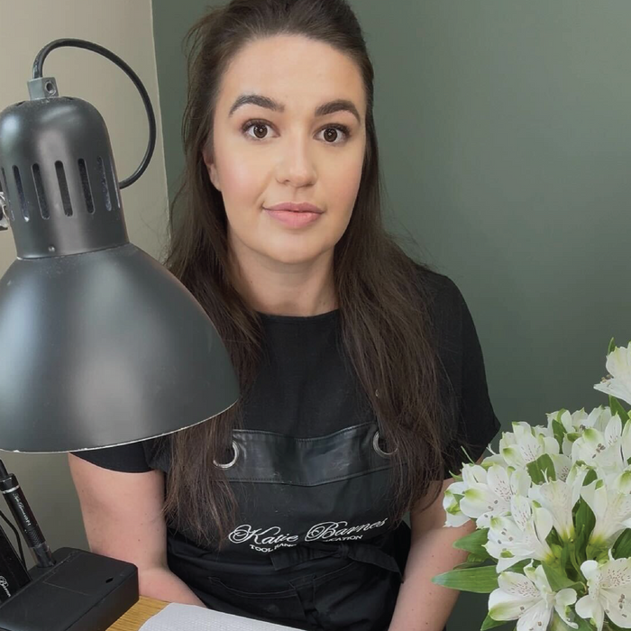 Woman sitting at a desk with a lamp and flowers in the foreground wearing Katie Barnes Tool Range apron.