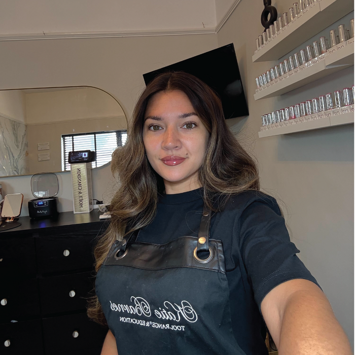 Woman wearing a black apron with Katie Barnes Tool Range logo in a room with shelves and a mirror.