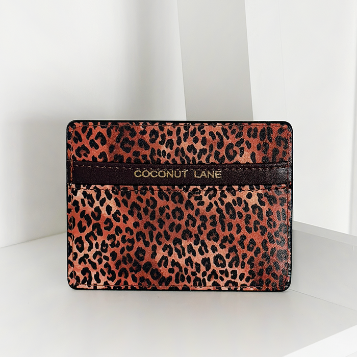 Leopard print vegan leather card holder with gold branding on a brown strip, shown on a white background.