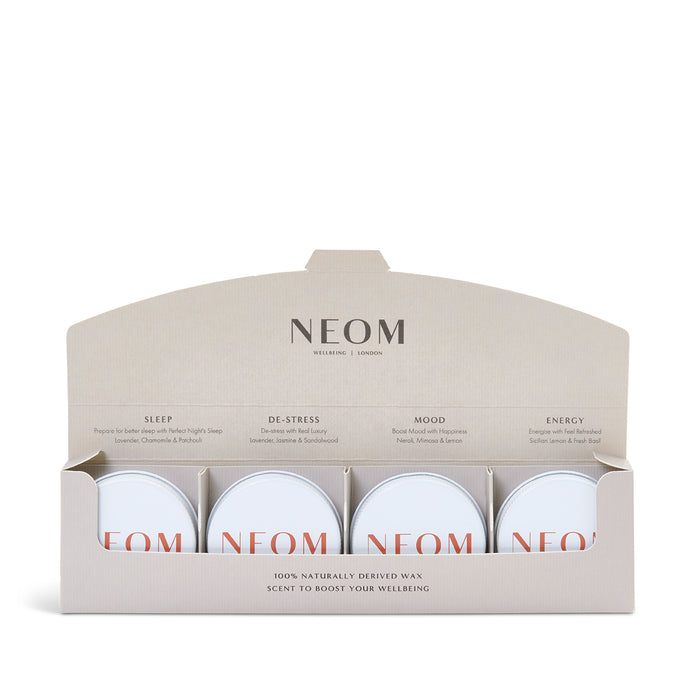 A set of four mini candles from NEOM, with labels indicating different scents such as 'Perfect Night’s Sleep', 'Real Luxury', 'Happiness', and 'Feel Refreshed'. The candles are presented in a sleek, minimalistic box with the NEOM branding.