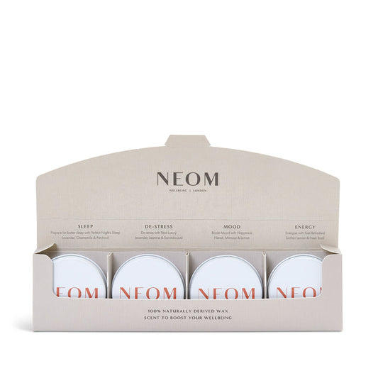A set of four mini candles from NEOM, with labels indicating different scents such as 'Perfect Night’s Sleep', 'Real Luxury', 'Happiness', and 'Feel Refreshed'. The candles are presented in a sleek, minimalistic box with the NEOM branding.