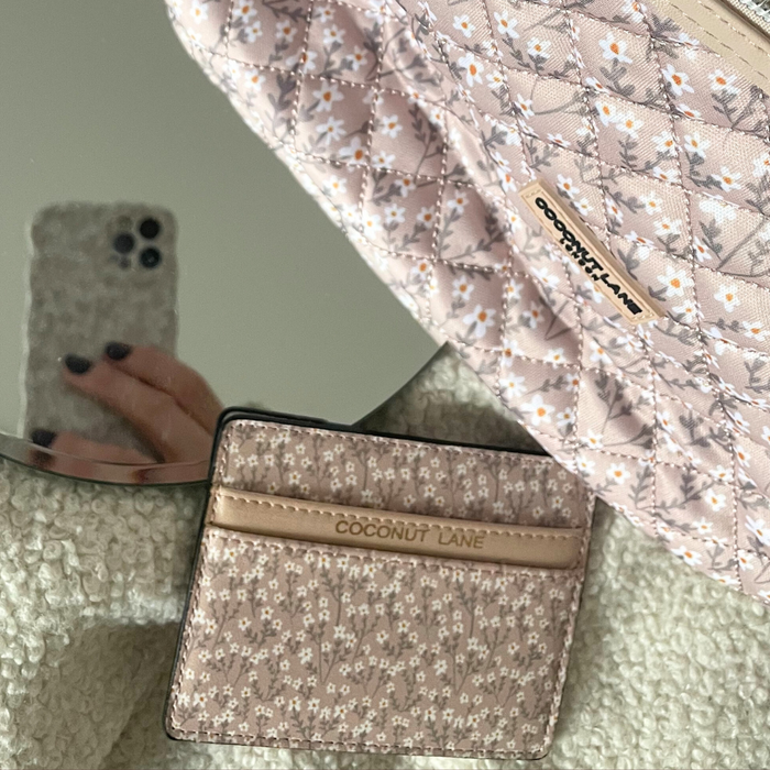 Beige floral Coconut Lane card holder and bag on a textured surface; hand with phone reflected in a mirror.