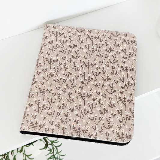 Beige floral Coconut Lane iPad case on a white surface beside a green plant.