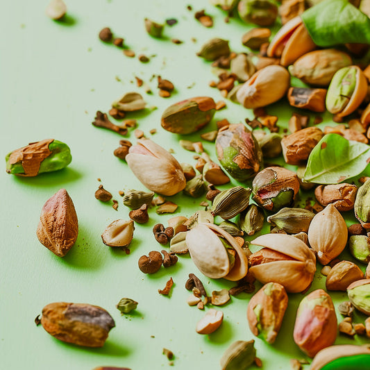 Scattered pistachio nuts and cardamom seeds on a green background