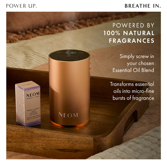 “Power Up. Breathe In"  NEOM diffuser on a bedside tray with essential oil bottle. Text reads: Powered by 100% natural fragrances. Simply screw in your chosen essential oil blend. Transforms essential oils into micro-fine bursts of fragrance.”