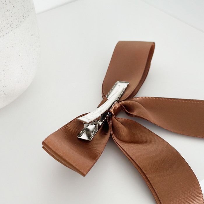 Brown ribbon bow hair clip by Coconut Lane displayed next to a white, textured vase.