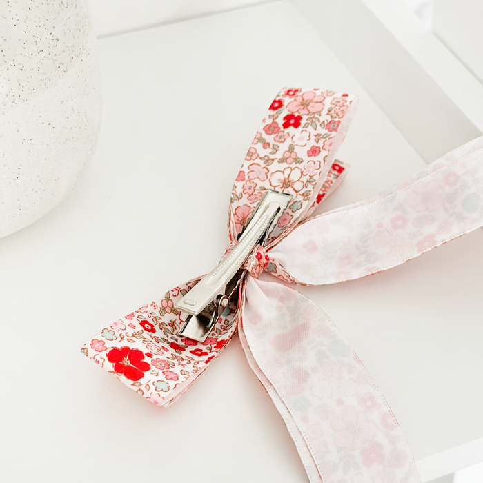 Floral-patterned Coconut Lane ribbon bow clip on a white surface next to a textured item.