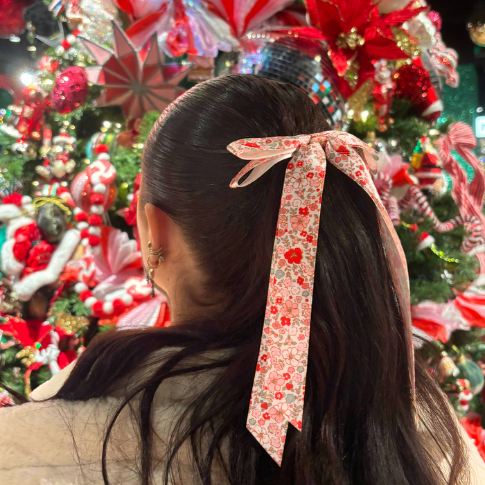 Woman with dark hair wearing a floral Coconut Lane ribbon bow clip, standing in front of festive holiday decorations.