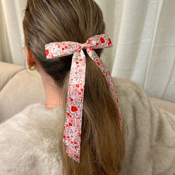 Woman with long hair wears a Coconut Lane ribbon bow clip featuring a cute floral pattern, seated on a beige couch.