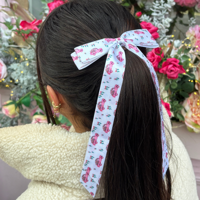 Woman with dark ponytail wears a pink Coconut Lane Ribbon Bow Clip, standing near pink flowers.