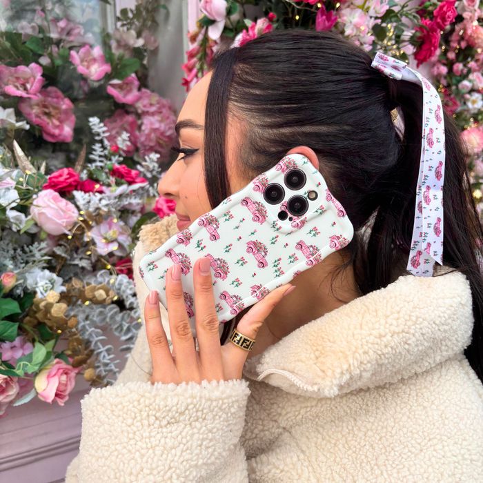 Woman with a Coconut Lane ribbon bow clip in her hair holds a floral phone near pink and white flowers.