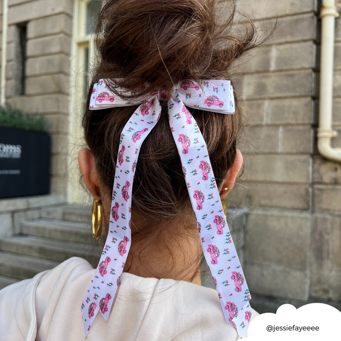 White satin ribbon bow clip with pink floral pattern, worn in a womans bun.