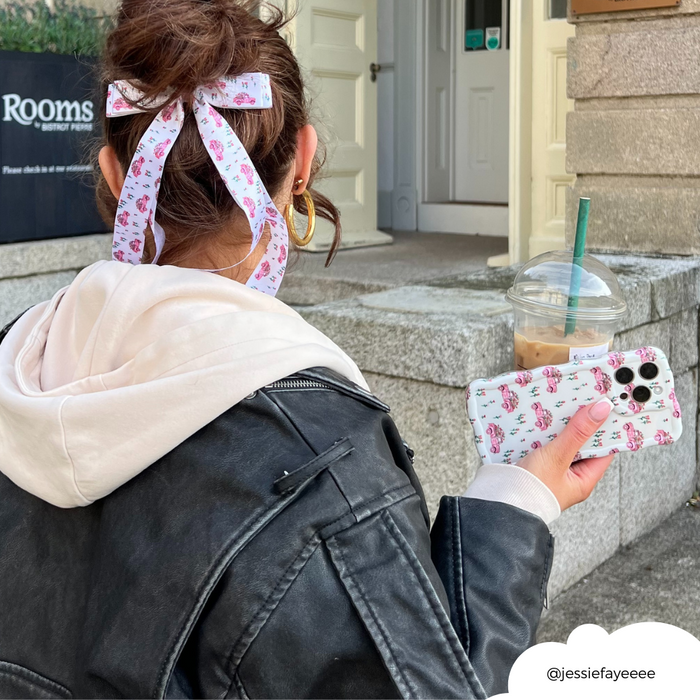Woman wearing Coconut Lane’s pink patterned ribbon bow clip and holding a matching phone case and iced coffee outdoors.