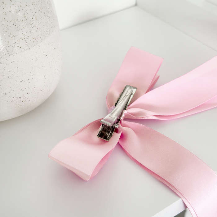 Peony pink ribbon bow clip on a white surface beside a speckled white vase.