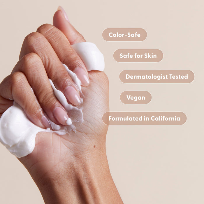 A hand squeezes white lotion from Arey’s Smooth Conditioner, with text bubbles reading: Color-Safe, Safe for Skin, Dermatologist Tested, Vegan, and Formulated in California—set against a neutral background to perfectly showcase this nourishing product.