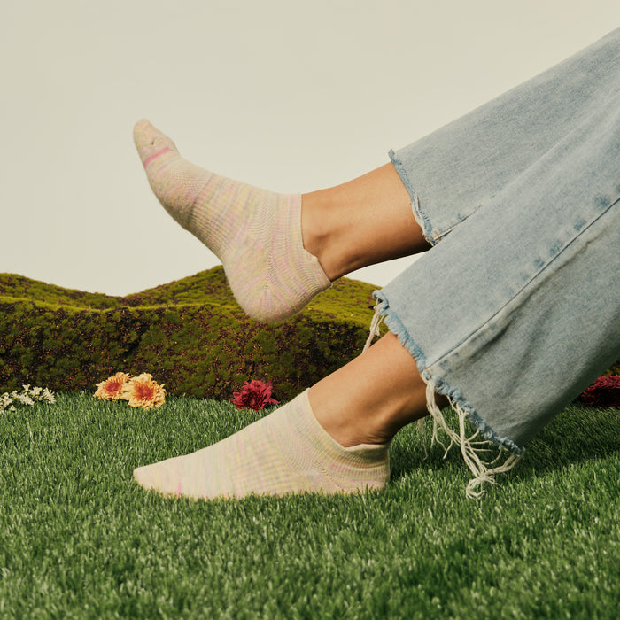 Ankle compression socks in pastel colors worn with frayed denim jeans, set against a grassy background with flowers.