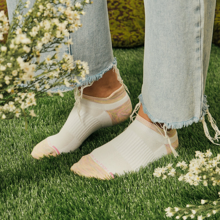 Ankle compression socks in white with pastel accents, worn with frayed denim jeans on grass.
