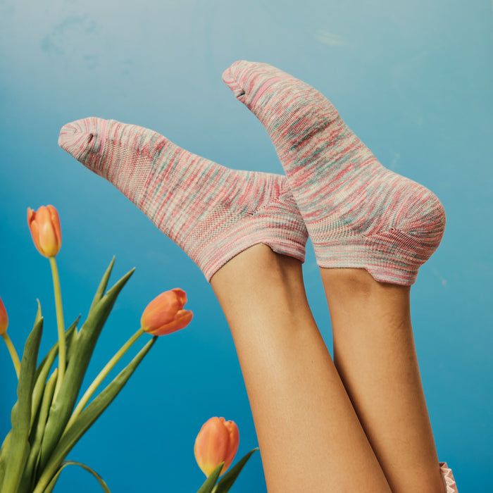 Ankle compression socks in pink and blue spacedye pattern, displayed with legs raised against a blue background and tulips.