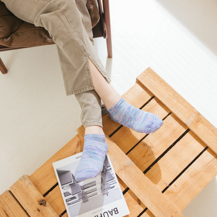 Ankle compression socks in purple and blue hues worn with light-colored pants, resting on a wooden surface.
