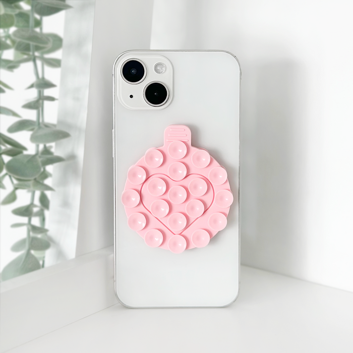 White smartphone with a pink Coconut Lane suction phone holder next to green leaves.