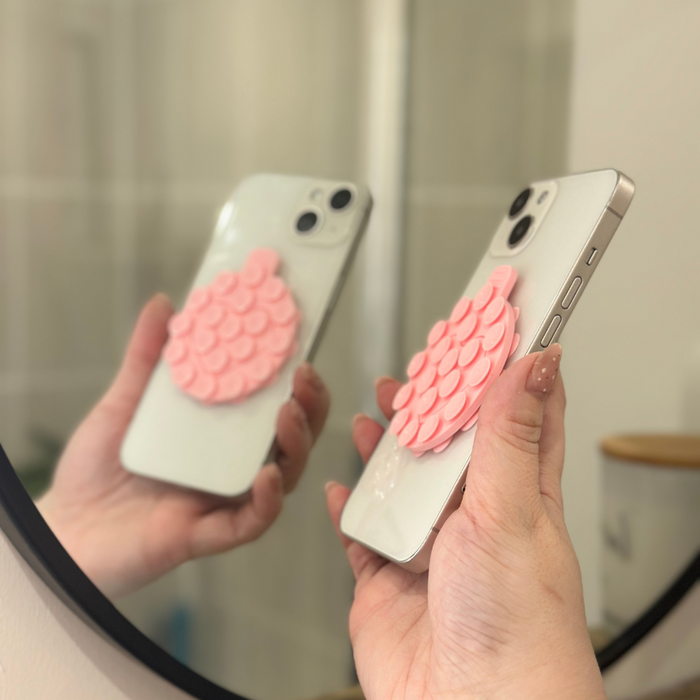Pink Coconut Lane suction phone holder on a phone, held in hand and reflected in a round mirror.