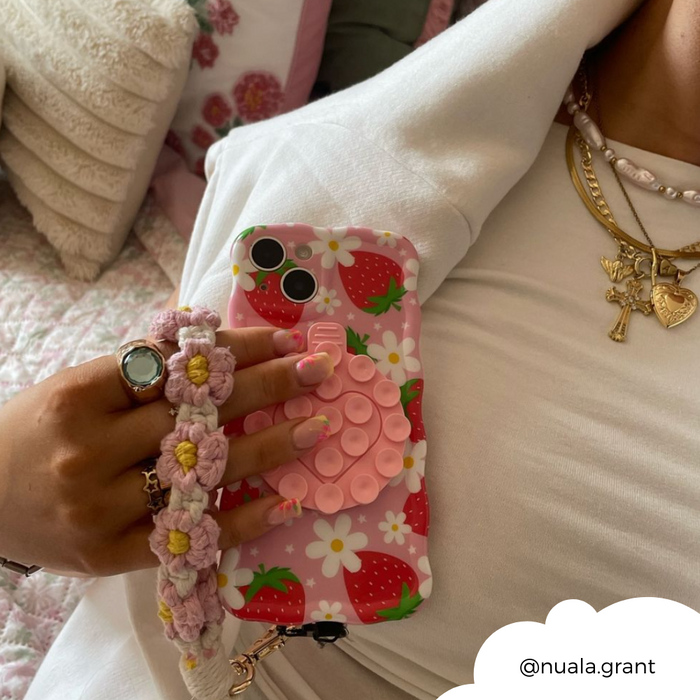 Phone in a pink strawberry case with floral strap, held by Coconut Lane Pink Suction Phone Holder.