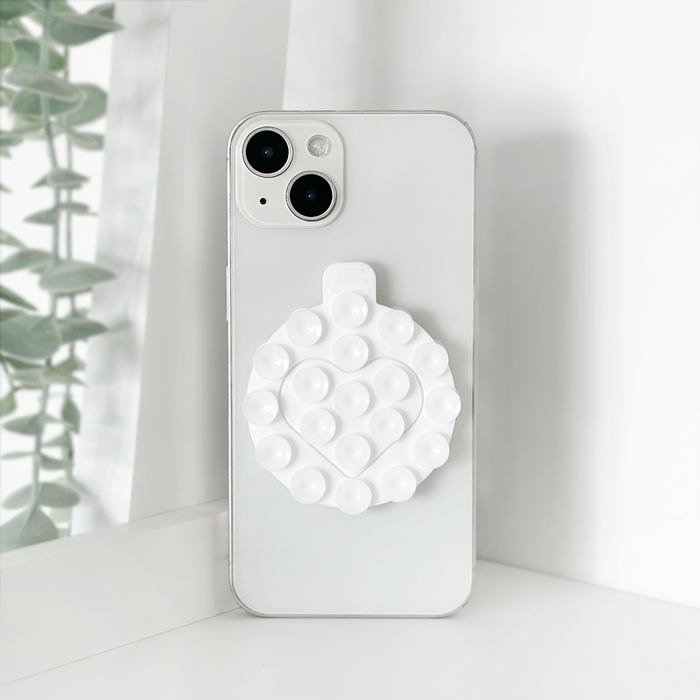 White Coconut Lane suction phone holder attached to a window, holding a phone with green leaves visible outside.