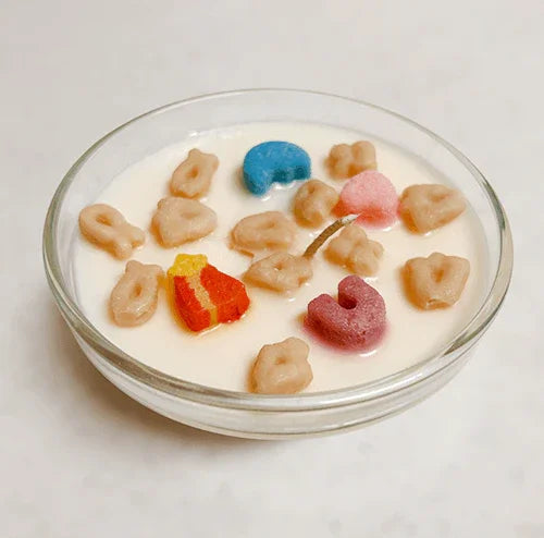 Cereal and colorful marshmallows in a glass bowl shaped candle with white wax resembling milk.