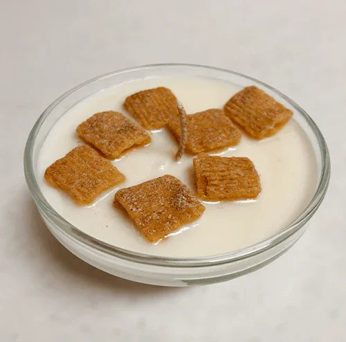 Cereal-shaped cinnamon pieces on creamy white candle in a glass bowl, dessert-inspired decor.