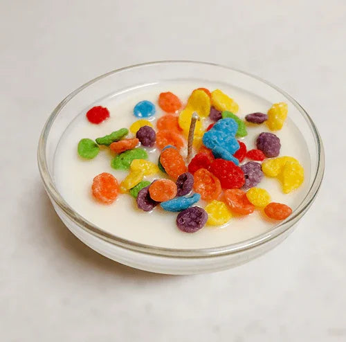 Fruity cereal-inspired candle in a glass bowl with colorful wax pieces on white surface.