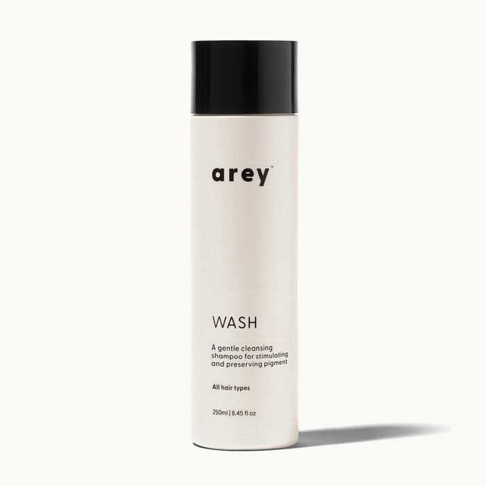 Arey Wash bottle on a cream background. Label reads: arey. WASH. A gentle cleansing shampoo for stimulating and preserving pigment. All hair types. 250ml / 8.45 fl oz.