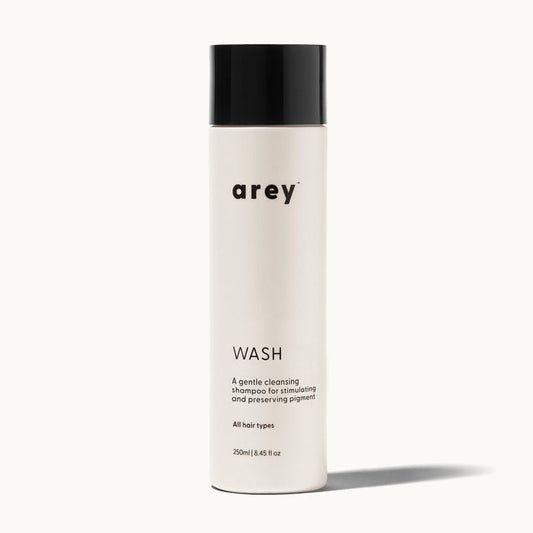 Arey Wash bottle on a cream background. Label reads: arey. WASH. A gentle cleansing shampoo for stimulating and preserving pigment. All hair types. 250ml / 8.45 fl oz.
