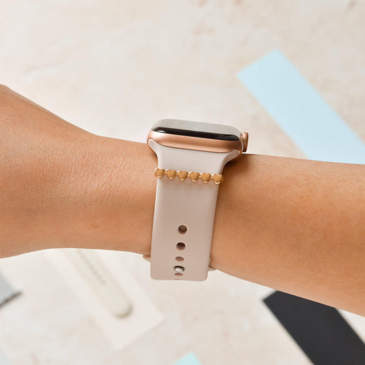 Gold heart watch strap charm on a beige smartwatch band with gold accents.