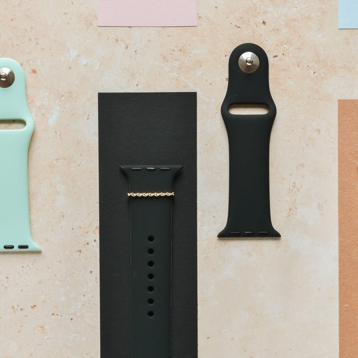 Three wristbands: mint green, plain black, and black with a gold twist charm, displayed on a beige surface.