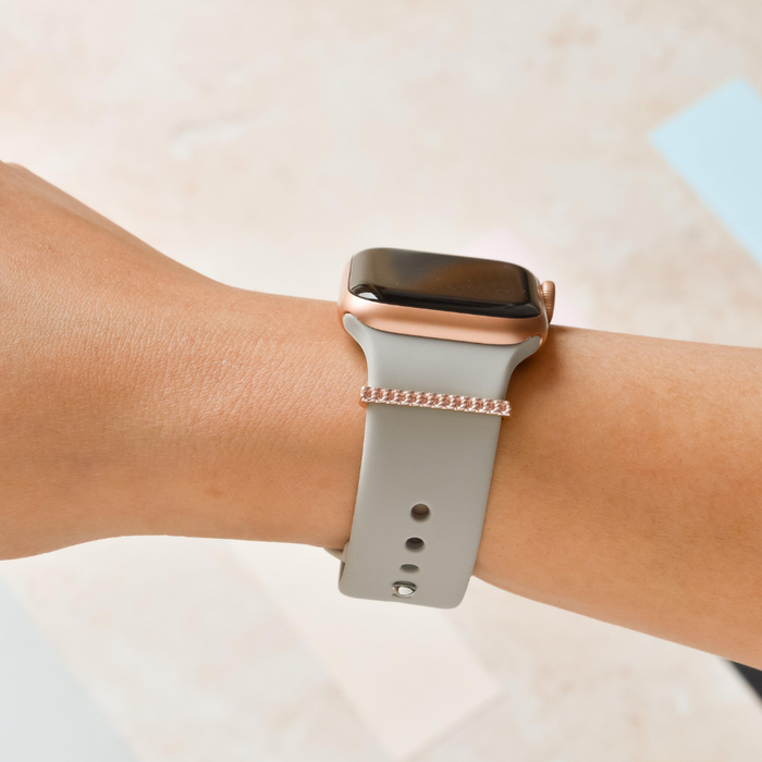 Light gray smartwatch with a rose gold strap charm on a wrist.