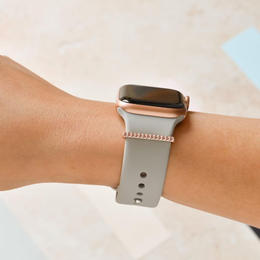 Light gray smartwatch with a rose gold strap charm on a wrist.