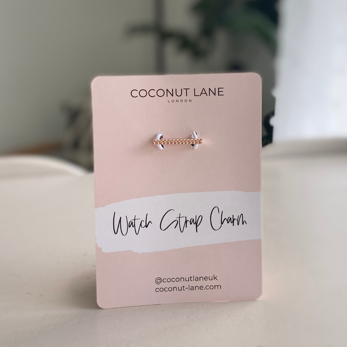 Rose gold watch strap charm on a pink card with Coconut Lane branding.