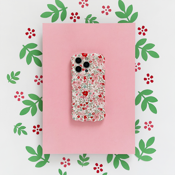 Wavy phone case with cute flower pattern, displayed on pink paper with green leaf and red flower cutouts.