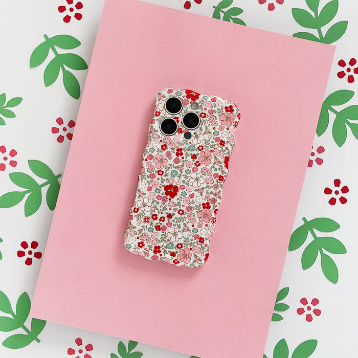Coconut Lane wavy phone case with colorful flower design on pink background, shown on floral-patterned paper.