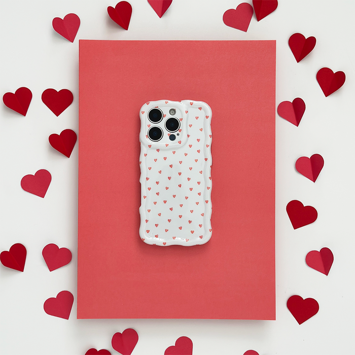Coconut Lane wavy phone case with mini hearts on pink paper, surrounded by scattered red paper hearts.